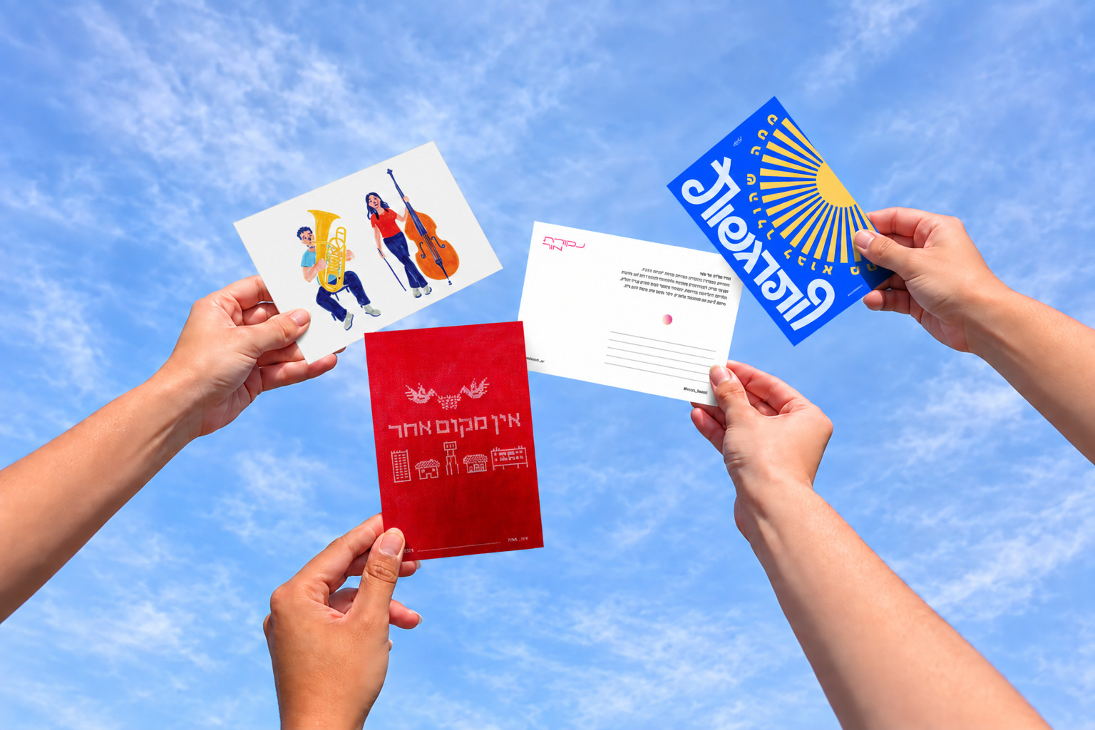 Hands holding Nekudat Or postcards against a blue sky